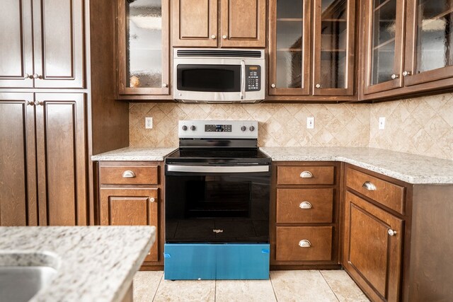 144 Lee Road 2083, Phenix City, AL 36870 - kitchen with stainless steel appliances, light tile patterned flooring, tasteful backsplash, brown cabinetry, and glass insert cabinets