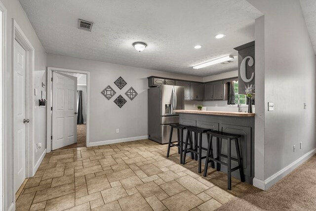 176 Lee Road 0504, Phenix City, AL 36870 - kitchen featuring stainless steel fridge with ice dispenser, a kitchen breakfast bar, light countertops, light stone finish floors, and a textured ceiling