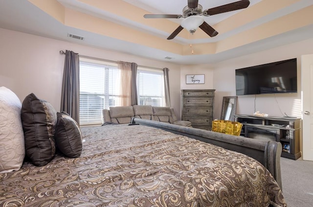 carpeted bedroom featuring ceiling fan and a raised ceiling