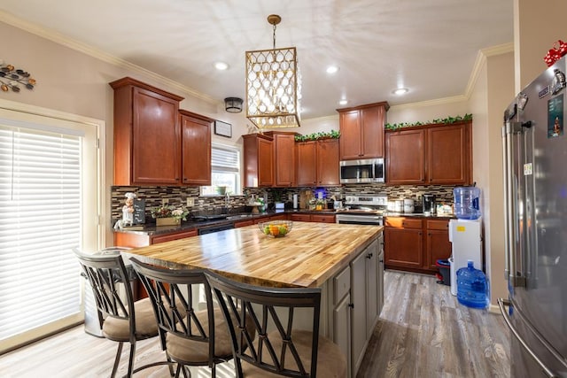 kitchen with pendant lighting, hardwood / wood-style flooring, crown molding, wooden counters, and stainless steel appliances