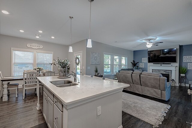 kitchen with ceiling fan, sink, hanging light fixtures, a fireplace, and a center island with sink