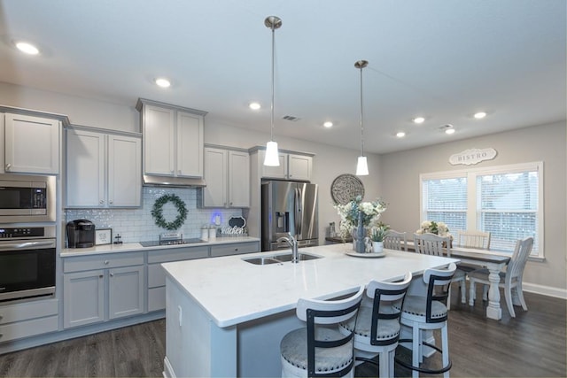 kitchen featuring gray cabinetry, stainless steel appliances, sink, pendant lighting, and an island with sink