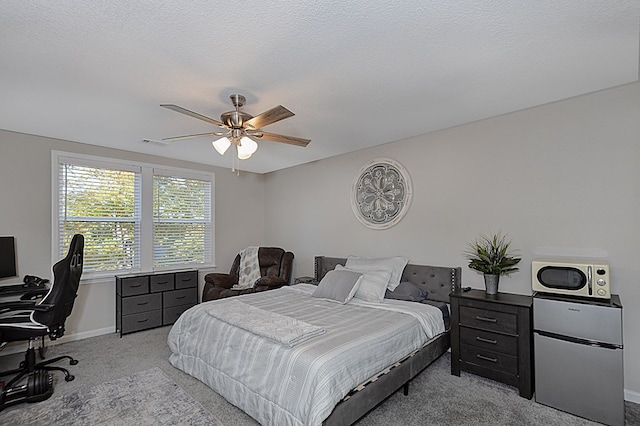 carpeted bedroom featuring ceiling fan, refrigerator, and a textured ceiling