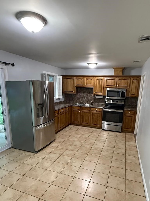 4229 Empire St, Columbus, GA 31907 - kitchen featuring stainless steel appliances, dark countertops, decorative backsplash, light tile patterned flooring, and brown cabinetry