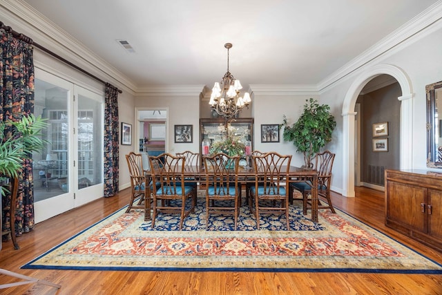 dining area featuring arched walkways, plenty of natural light, wood finished floors, and crown molding