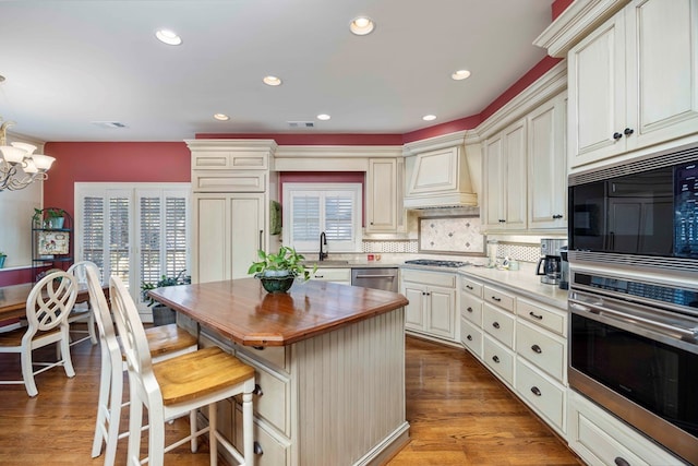 kitchen featuring tasteful backsplash, custom range hood, stainless steel dishwasher, wood counters, and a sink