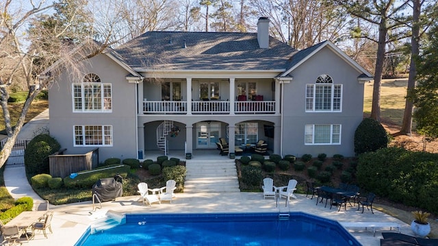 rear view of property with stairway, stucco siding, a chimney, an outdoor pool, and a patio