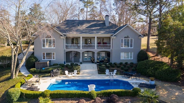 rear view of property featuring an outdoor pool, stucco siding, a patio, and a balcony