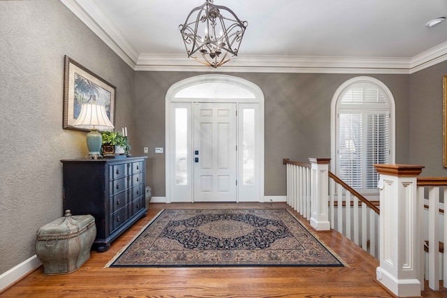 entrance foyer with baseboards, a notable chandelier, wood finished floors, and crown molding