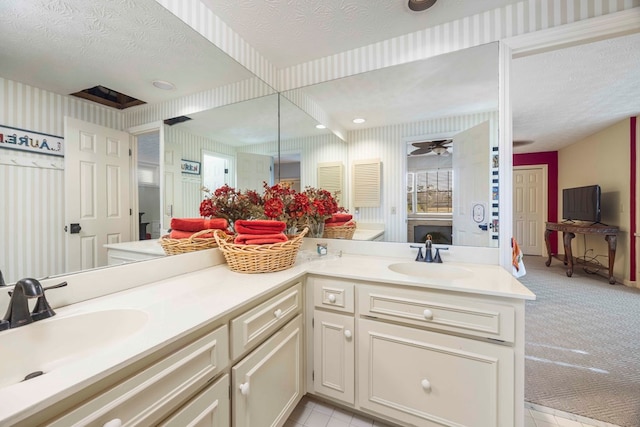 bathroom with double vanity, wallpapered walls, a textured ceiling, and a sink