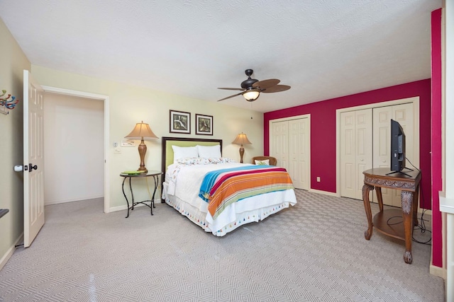 carpeted bedroom with baseboards, multiple closets, a textured ceiling, and a ceiling fan