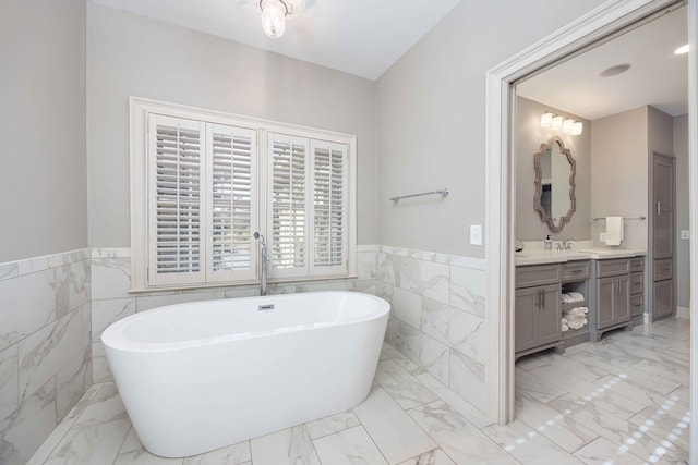 full bath with vanity, a freestanding tub, marble finish floor, and wainscoting