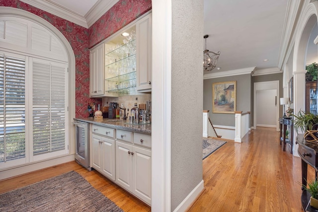 bar featuring baseboards, wine cooler, ornamental molding, light wood-style flooring, and a notable chandelier