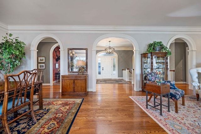 foyer entrance with arched walkways, ornamental molding, baseboards, and wood finished floors