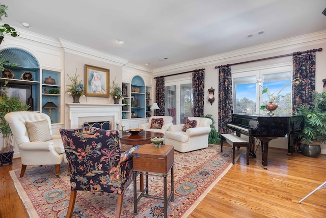 living area featuring light wood finished floors, visible vents, a fireplace, and crown molding