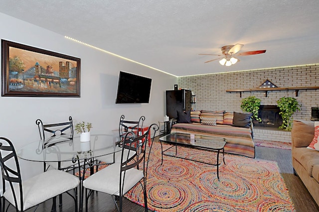 living area featuring wood finished floors, ceiling fan, brick wall, and a brick fireplace