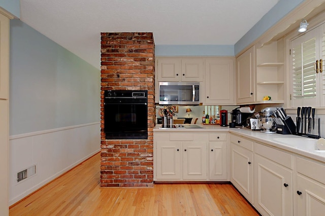 kitchen featuring black oven, stainless steel microwave, open shelves, light wood-type flooring, and light countertops