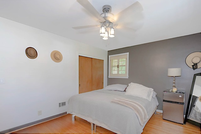 bedroom featuring light wood-style floors, freestanding refrigerator, a closet, baseboards, and ceiling fan