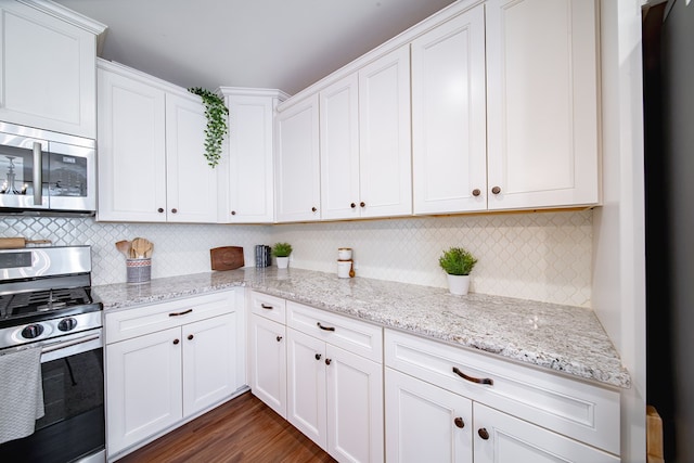 kitchen featuring white cabinetry, tasteful backsplash, light stone counters, appliances with stainless steel finishes, and dark hardwood / wood-style floors