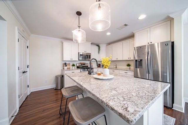 kitchen with pendant lighting, appliances with stainless steel finishes, light stone countertops, and a kitchen island with sink