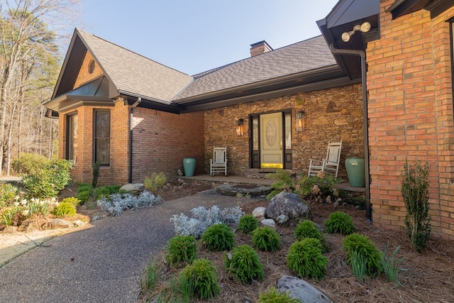 exterior space featuring brick siding, stone siding, a chimney, and a shingled roof