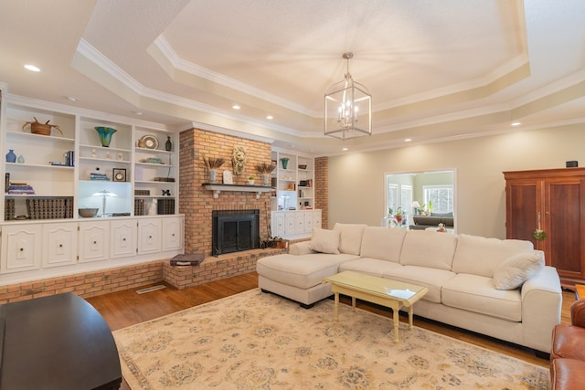 living room featuring a fireplace, a tray ceiling, crown molding, and wood finished floors