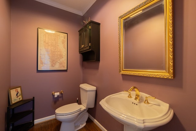 half bathroom featuring crown molding, baseboards, toilet, wood finished floors, and a sink