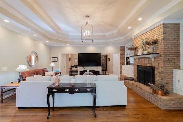 living room featuring ornamental molding, a brick fireplace, a tray ceiling, and wood finished floors