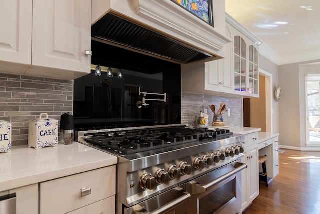 kitchen with crown molding, glass insert cabinets, premium range hood, range with two ovens, and wood finished floors