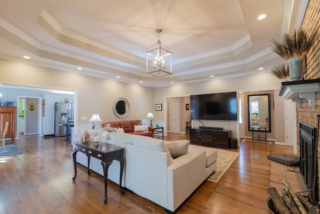 living area featuring a tray ceiling, a brick fireplace, and wood finished floors