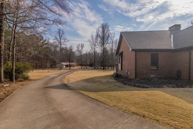 view of side of property with a yard, brick siding, roof with shingles, and a chimney