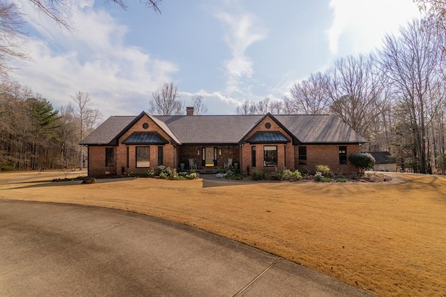 view of front facade with a front yard, brick siding, and a chimney