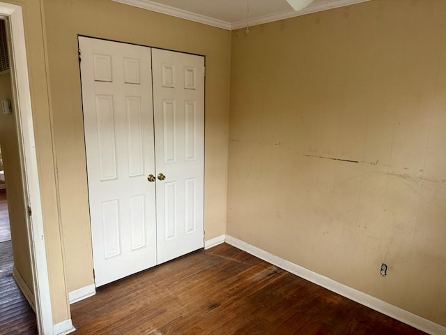 unfurnished bedroom with dark wood-type flooring, ornamental molding, and a closet