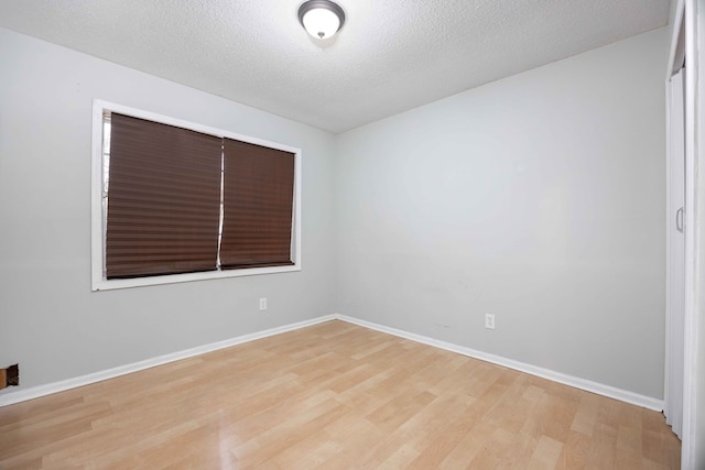 empty room featuring light wood finished floors, baseboards, and a textured ceiling