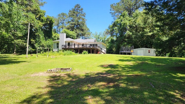 4232 Almond Rd, Fortson, GA 31808 - view of grassy yard featuring a fire pit, a deck, a trampoline, and an outbuilding