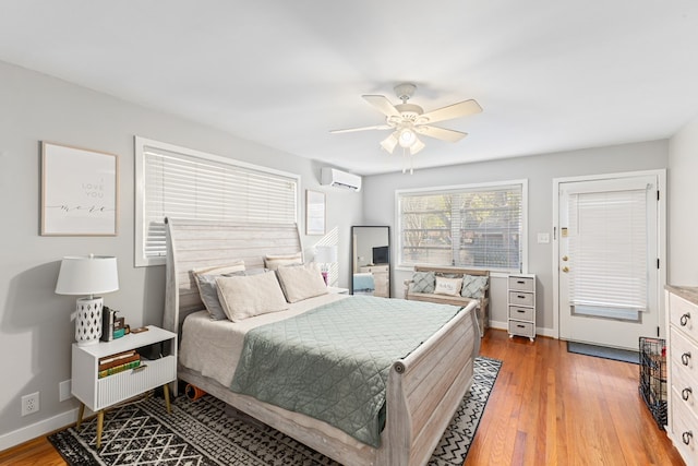 bedroom featuring a wall unit AC, ceiling fan, baseboards, and wood finished floors