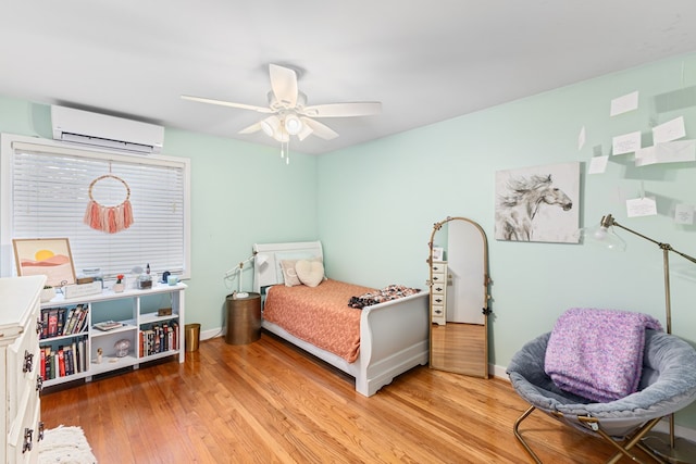 bedroom featuring a ceiling fan, a wall unit AC, light wood-style flooring, and baseboards