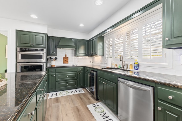 kitchen featuring stainless steel appliances, a sink, beverage cooler, premium range hood, and green cabinetry