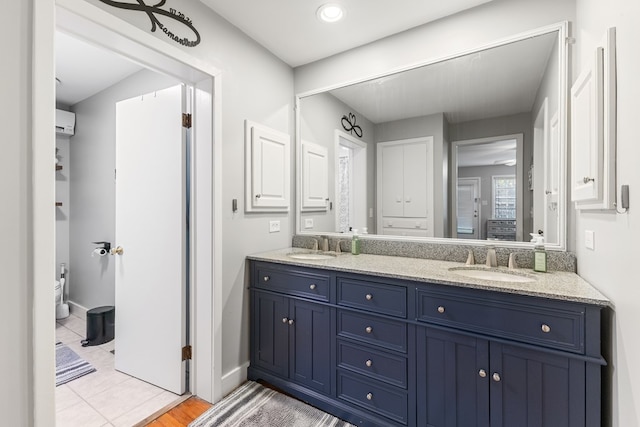 bathroom with double vanity, a wall mounted air conditioner, a sink, and baseboards