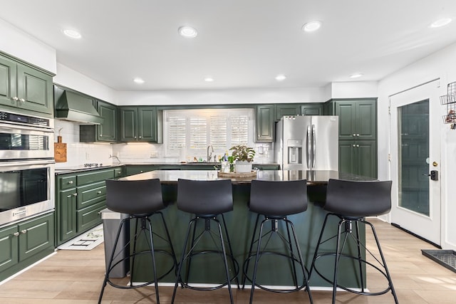 kitchen featuring a center island, tasteful backsplash, custom range hood, green cabinets, and appliances with stainless steel finishes