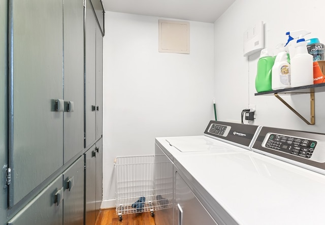 clothes washing area with cabinet space, wood finished floors, and washing machine and clothes dryer