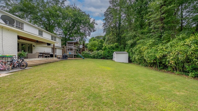 view of grassy yard with a playground, a shed, a ceiling fan, and an outbuilding