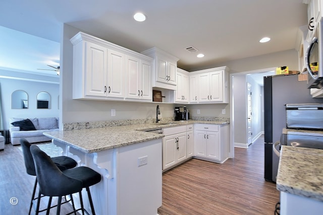 kitchen with sink, dark wood-type flooring, white cabinetry, light stone countertops, and a breakfast bar