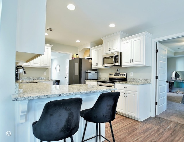 kitchen with white cabinets, a kitchen bar, stainless steel appliances, light hardwood / wood-style floors, and sink