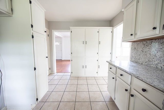 kitchen with tasteful backsplash, light stone countertops, white cabinetry, and light tile patterned floors