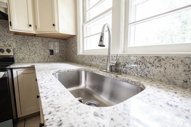 details with tasteful backsplash, stainless steel electric range oven, light stone counters, and a sink