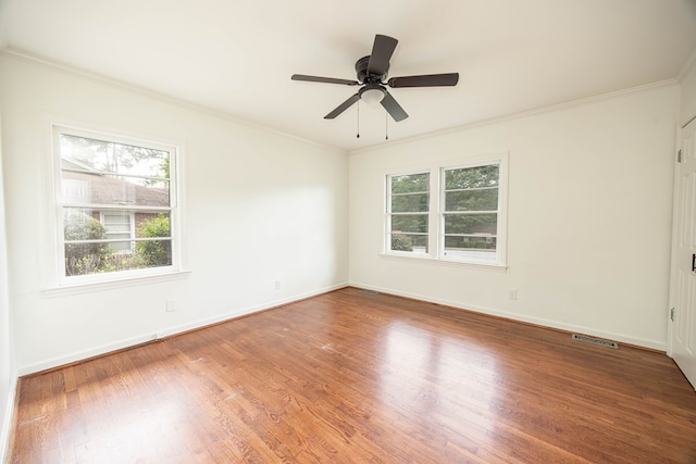 empty room with baseboards, visible vents, wood finished floors, ceiling fan, and crown molding