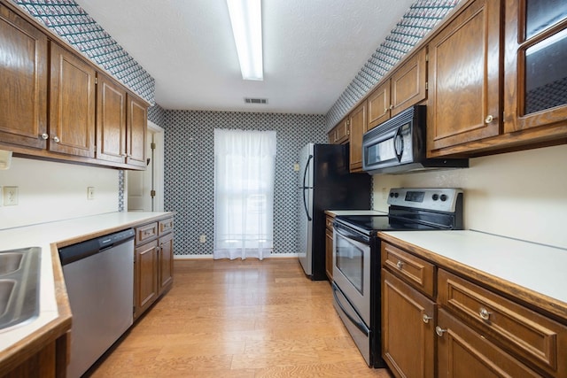 4608 Mayo Dr, Columbus, GA 31909 - kitchen featuring stainless steel appliances, wallpapered walls, light countertops, light wood-style flooring, and brown cabinetry