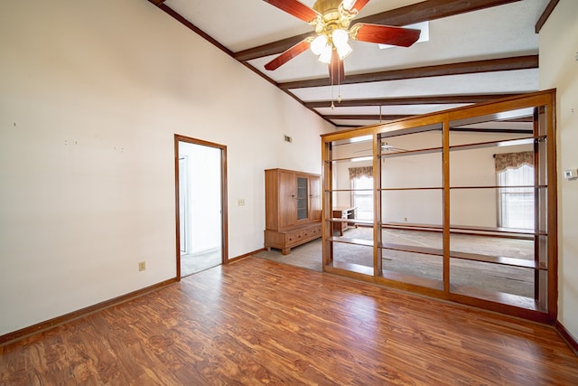 unfurnished room featuring baseboards, a ceiling fan, beamed ceiling, wood finished floors, and high vaulted ceiling