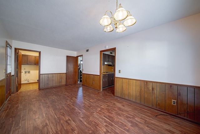 spare room with visible vents, dark wood finished floors, wainscoting, an inviting chandelier, and a textured ceiling